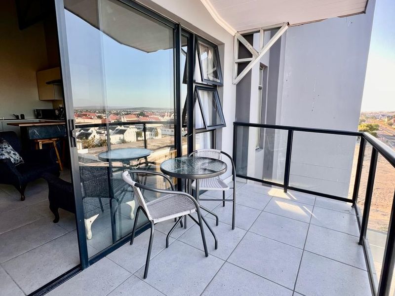 A modern balcony featuring tiled flooring, a sleek glass balustrade, and large sliding doors that provide seamless access to the interior living space.