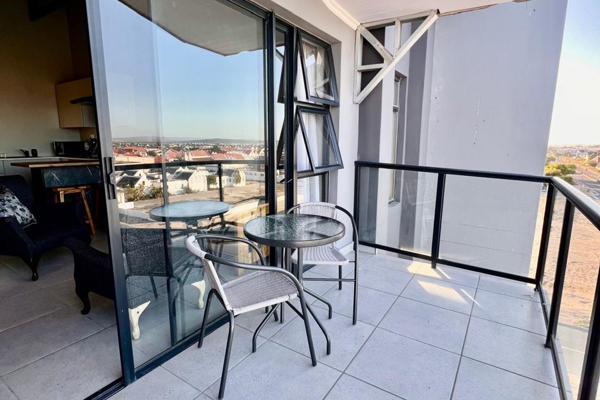 A modern balcony featuring tiled flooring, a sleek glass balustrade, and large sliding doors that provide seamless access to the interior living space.