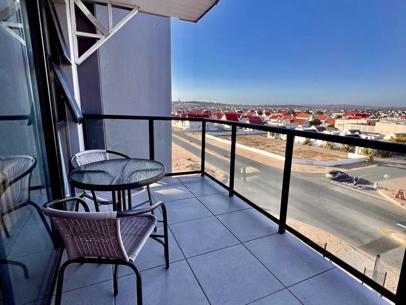 A modern covered balcony featuring tiled flooring and a sleek glass balustrade, offering expansive views of the surrounding neighborhood.