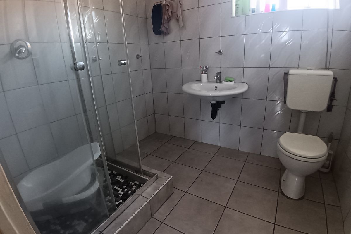 A functional bathroom featuring a glass-enclosed shower, wall-mounted basin, and standard toilet with tiled finishes throughout.