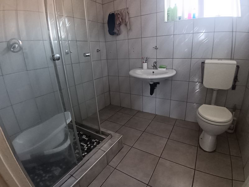 A functional bathroom featuring a glass-enclosed shower, wall-mounted basin, and standard toilet with tiled finishes throughout.