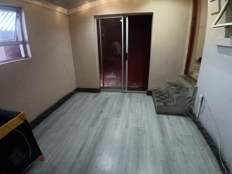 An empty living area featuring laminate flooring, a sliding glass door, and tiled steps leading to an adjacent space.