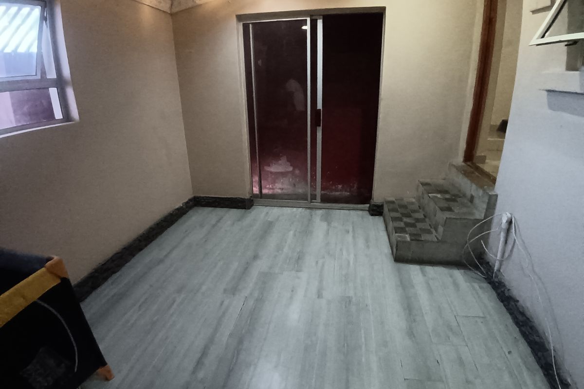 An empty living area featuring laminate flooring, a sliding glass door, and tiled steps leading to an adjacent space.