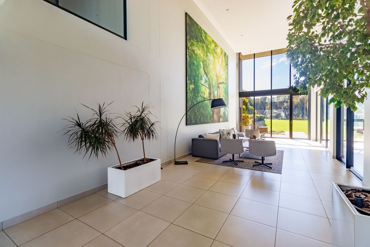 Spacious, light-filled living area featuring double volume ceilings, large floor-to-ceiling windows, and neutral tiled flooring with direct access to the garden.