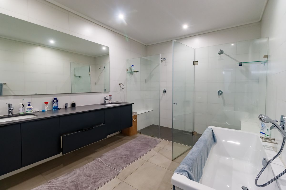 Modern bathroom featuring a double vanity, large wall-to-wall mirror, spacious walk-in shower with glass screen, and a separate freestanding bathtub.
