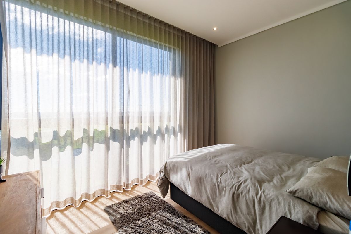 A bright and modern bedroom featuring floor-to-ceiling curtains and a large sliding glass door that provides ample natural light.