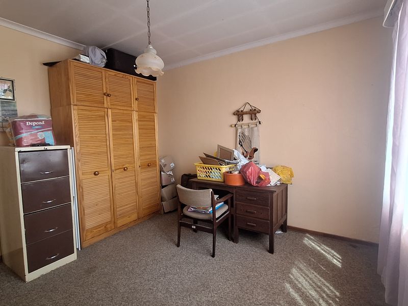 A bedroom featuring a built-in wooden wardrobe, carpeted flooring, and a central pendant light fixture.