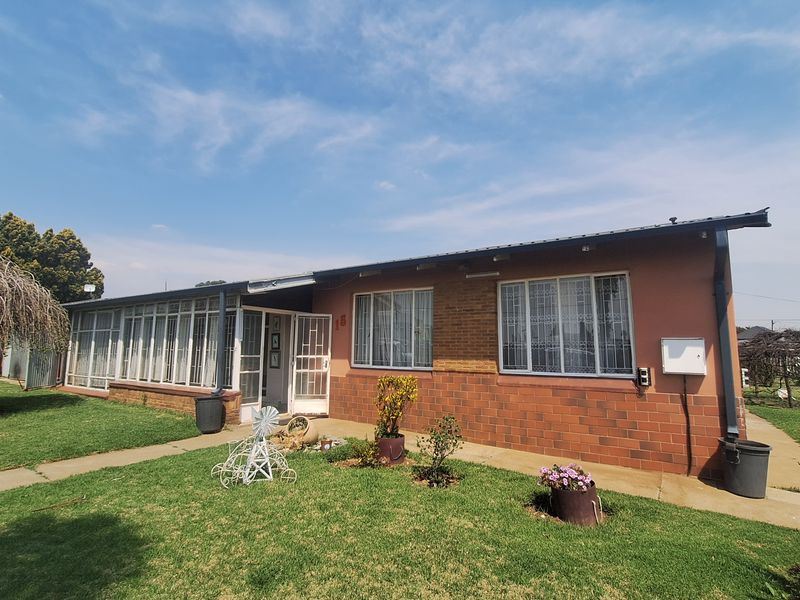 Front elevation of a single-story brick house featuring a metal roof, aluminium window frames, and a paved walkway leading to the entrance.