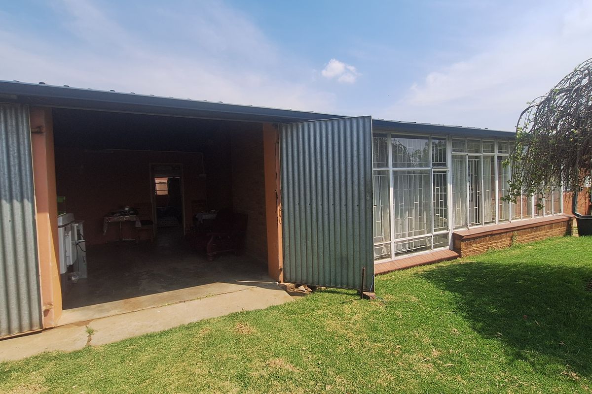 Rear view of the property featuring a large open garage area with corrugated metal siding and extensive glass window panels overlooking the garden.