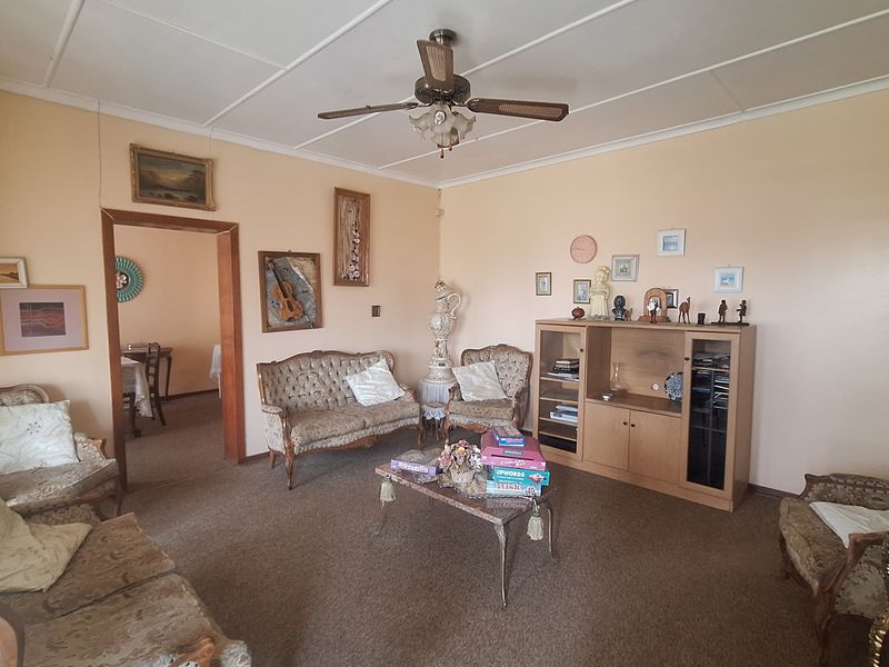 A spacious living room featuring a ceiling fan and exposed beam ceiling, offering a traditional layout with direct access to an adjacent dining area.
