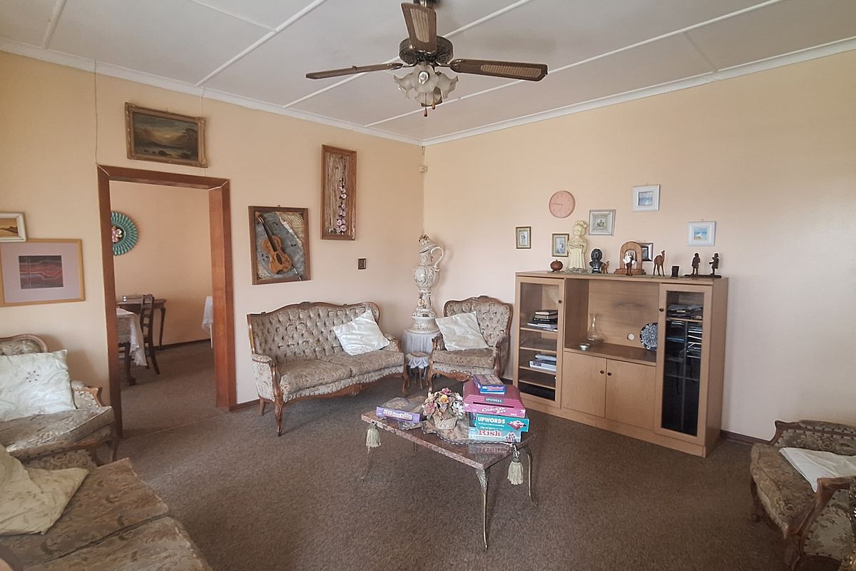 A spacious living room featuring a ceiling fan and exposed beam ceiling, offering a traditional layout with direct access to an adjacent dining area.
