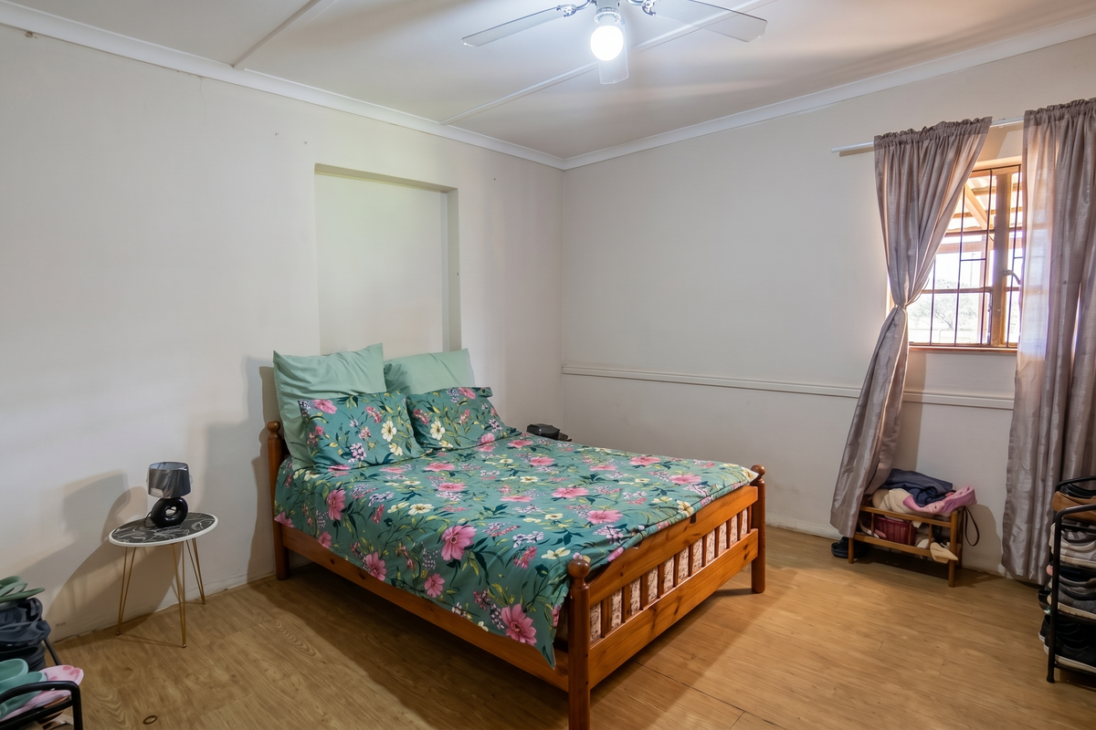 A functional bedroom featuring laminate flooring, a ceiling fan, and a window with security bars, offering a neutral base for personalization.