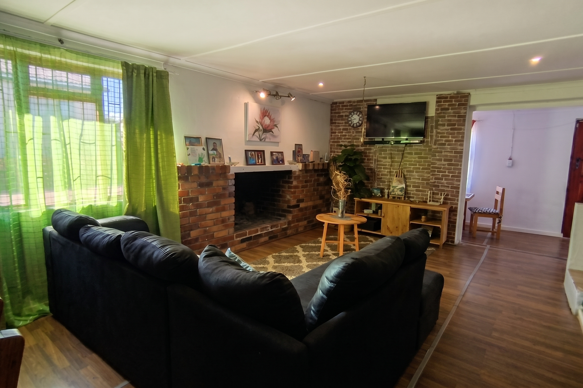 A cozy living room featuring a prominent brick fireplace and matching brick feature wall, complemented by warm laminate flooring and recessed lighting.