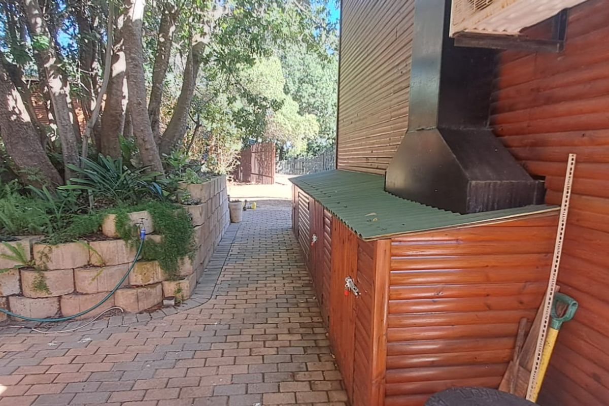 A side pathway featuring brick paving, a timber-clad exterior wall, a retaining wall, and an external chimney structure.