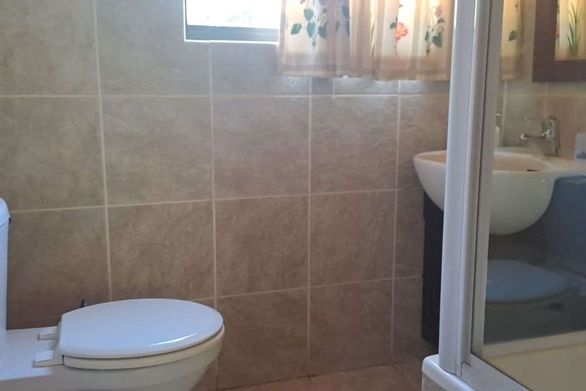 A functional bathroom featuring tiled walls, a standard toilet, a vanity basin, and a shower enclosure.