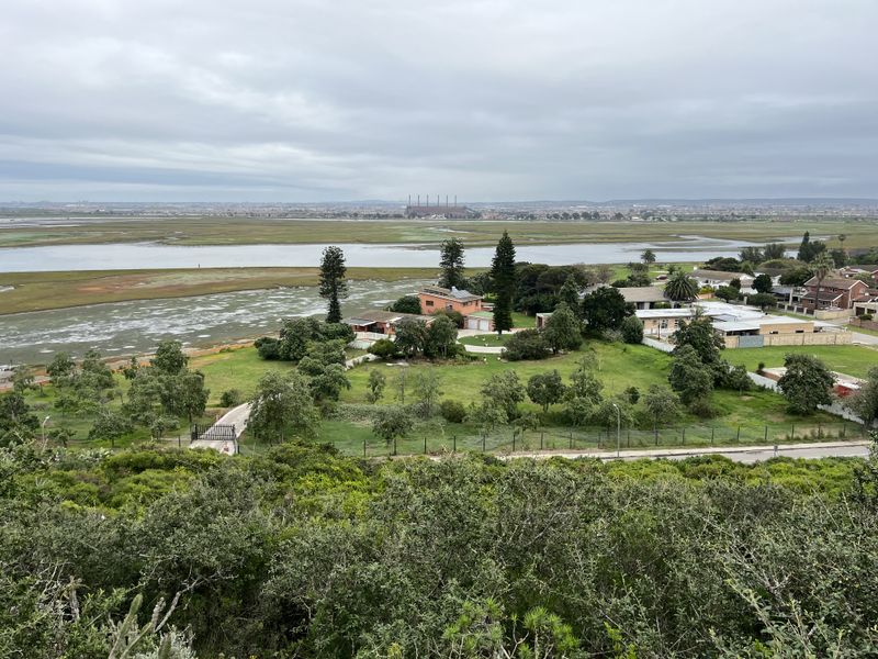 An elevated aerial view of a residential property featuring a large garden, driveway, and surrounding landscape with water views.