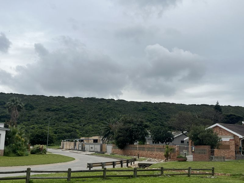 A street view of a residential area featuring paved roads, brick boundary walls, and established landscaping with a scenic hillside backdrop.