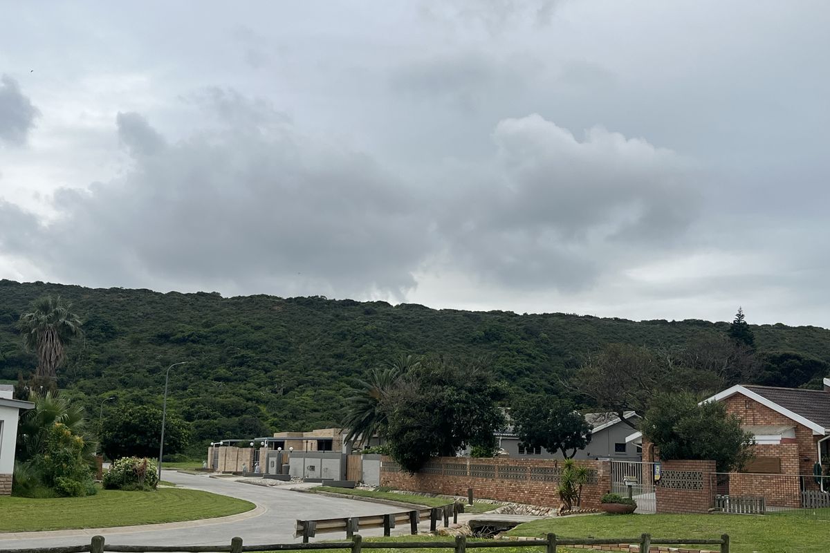 A street view of a residential area featuring paved roads, brick boundary walls, and established landscaping with a scenic hillside backdrop.