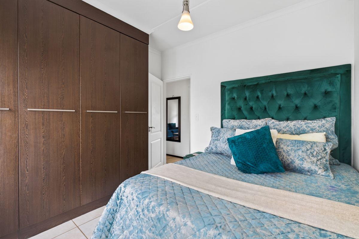 A well-maintained bedroom featuring dark wood built-in wardrobes and tiled flooring, offering a clean and functional living space.