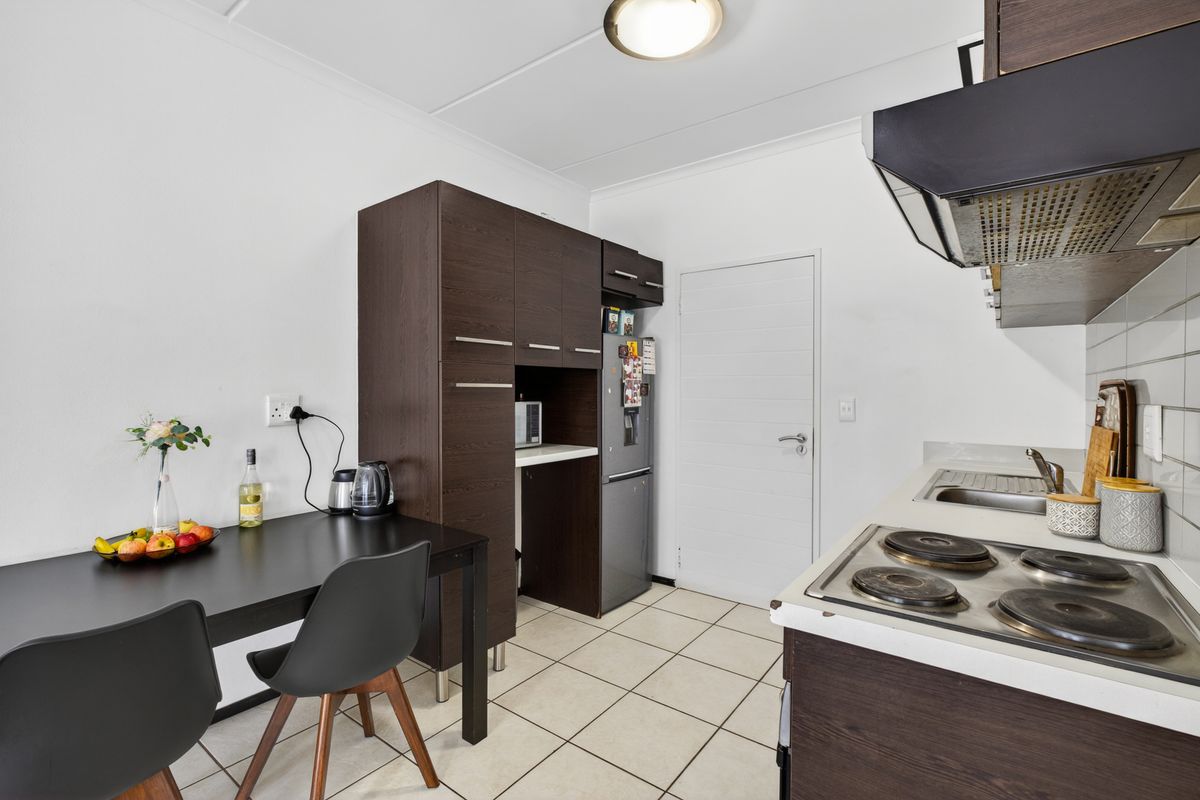 A functional kitchen featuring dark wood cabinetry, a built-in electric hob with extractor fan, tiled backsplash, and neutral floor tiles.