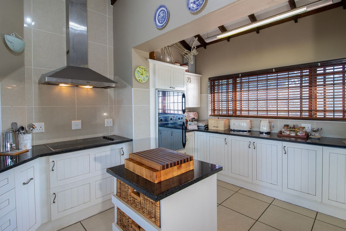 A well-maintained kitchen featuring white cabinetry, granite countertops, a built-in oven, extractor fan, and exposed timber ceiling beams.