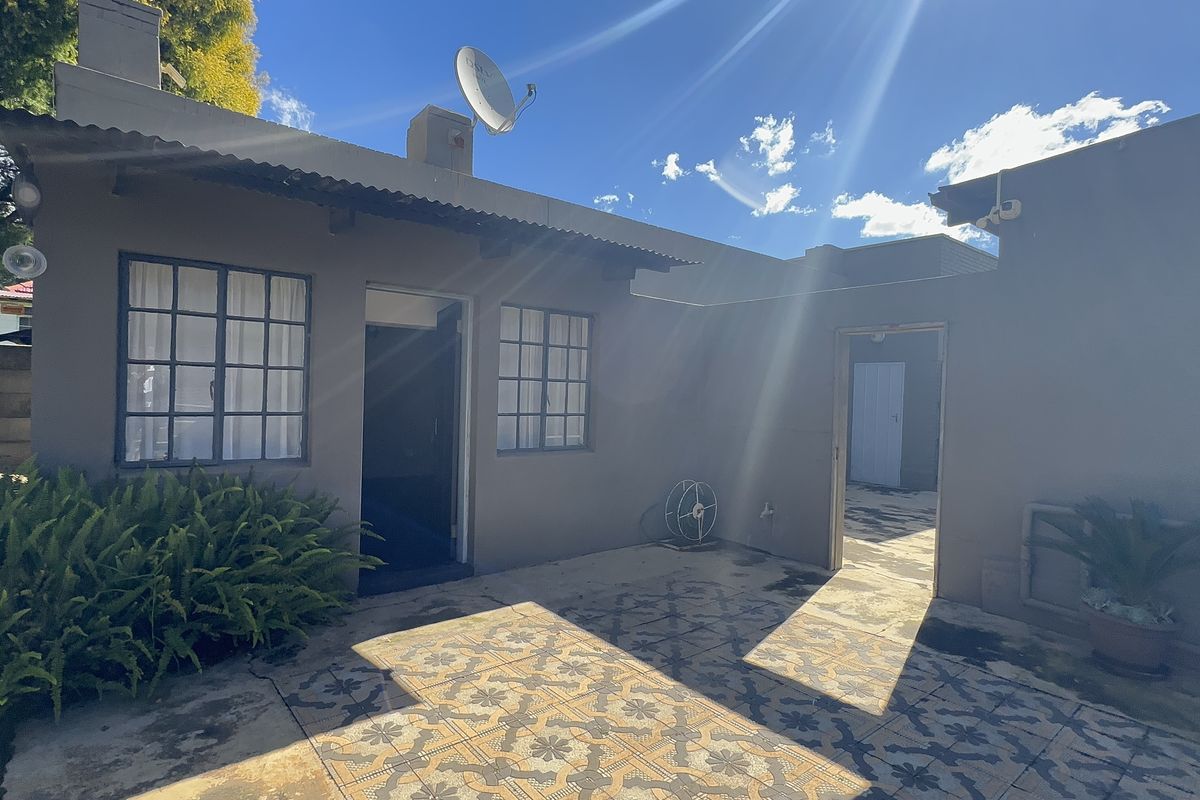 Rear exterior view of the property featuring a paved patio area, corrugated roof, and access points to the main dwelling.