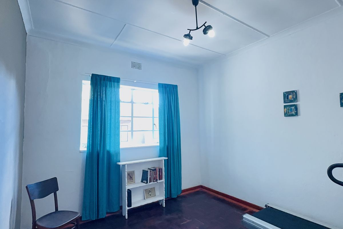 A bedroom featuring timber flooring, a steel-framed window, and a central ceiling light fixture, offering a functional space with potential for cosmetic updates.