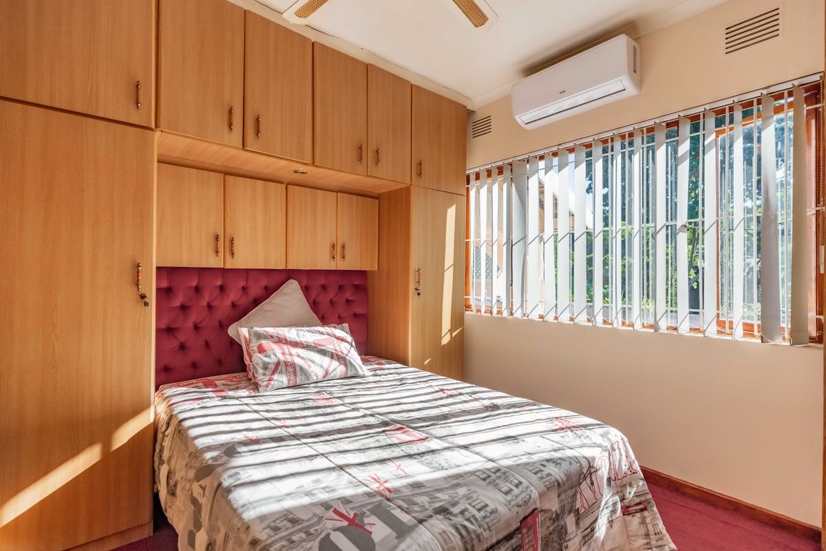 A bedroom featuring extensive built-in wooden cabinetry, a wall-mounted air conditioning unit, and security burglar bars on the window.