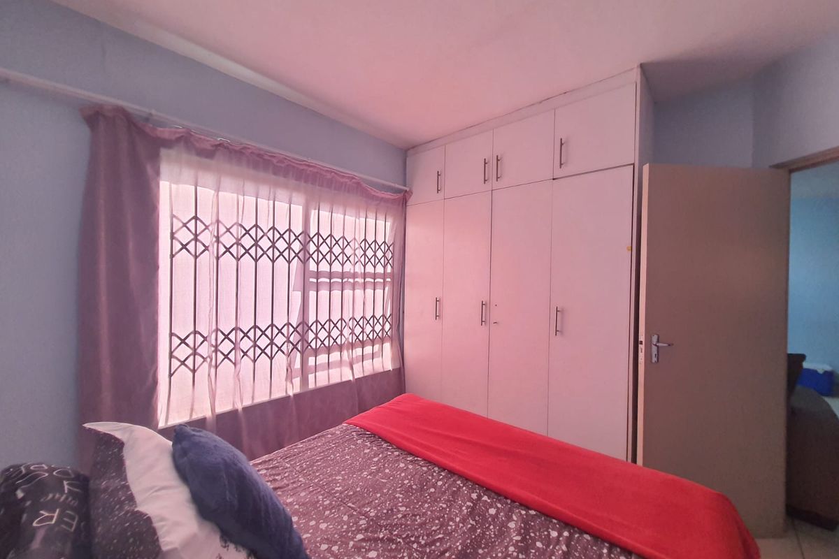 A bedroom featuring built-in cupboards and a window fitted with a security gate, offering functional storage and natural light.