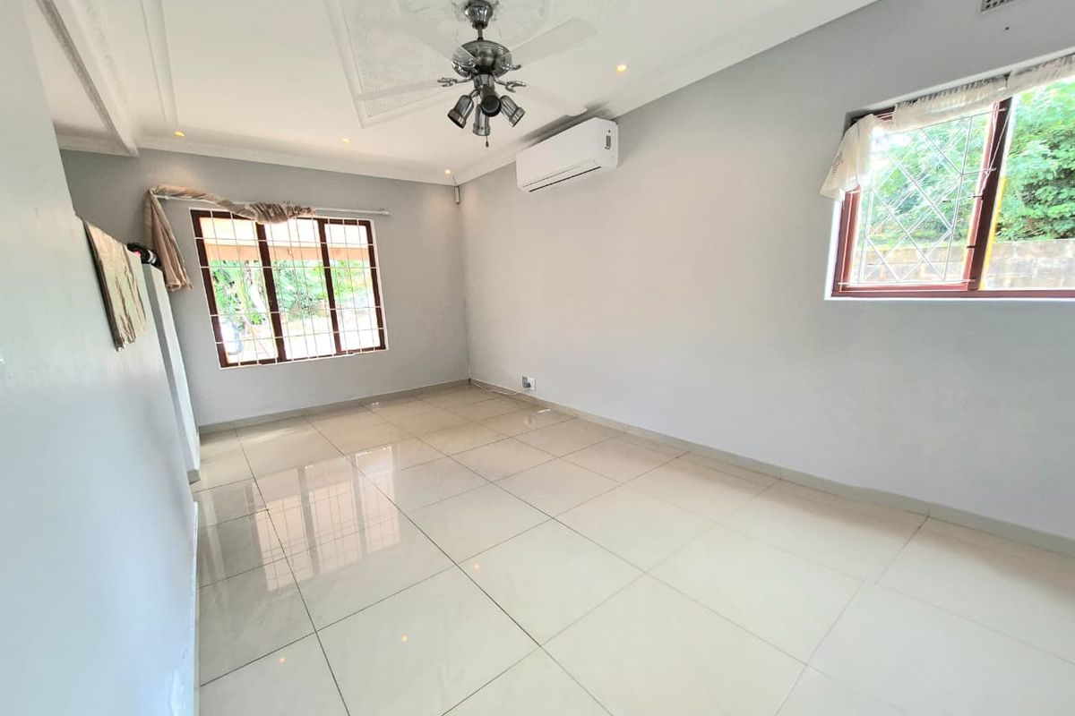 A bright, empty living room featuring polished porcelain floor tiles, a ceiling fan, and a wall-mounted air conditioning unit.