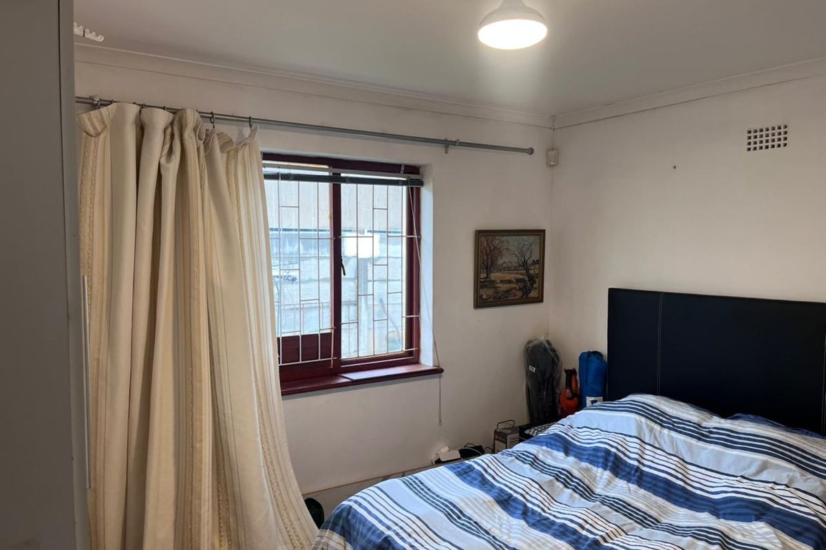 A functional bedroom featuring a window with security bars and standard ceiling lighting.