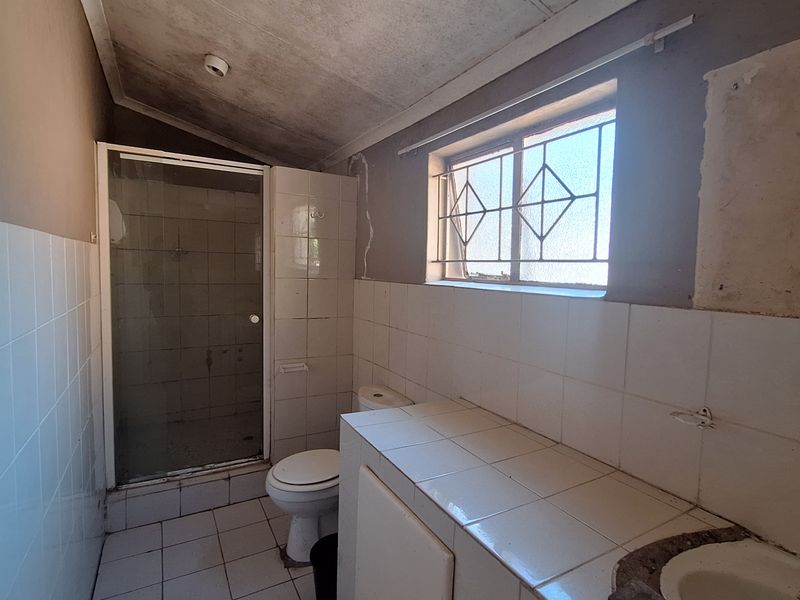 A dated bathroom featuring a shower enclosure, toilet, and tiled vanity. The space requires significant renovation and cosmetic updates to improve its condition.