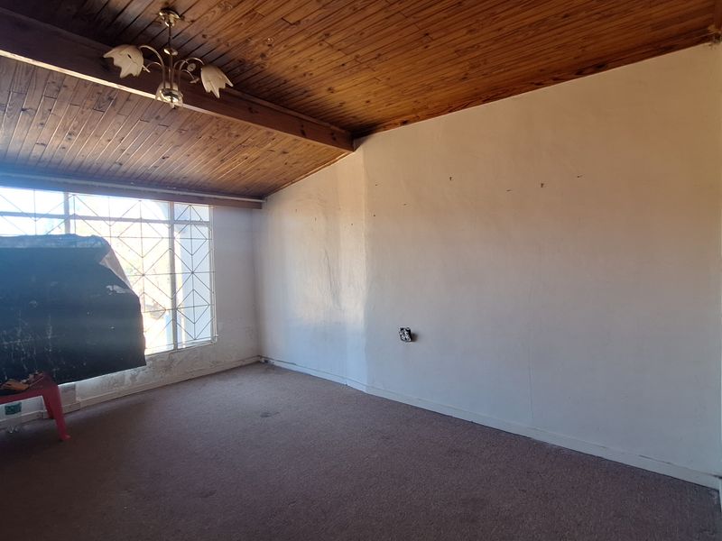 An empty living room featuring a timber-clad ceiling with exposed beams, carpeted flooring, and a security gate over the window.