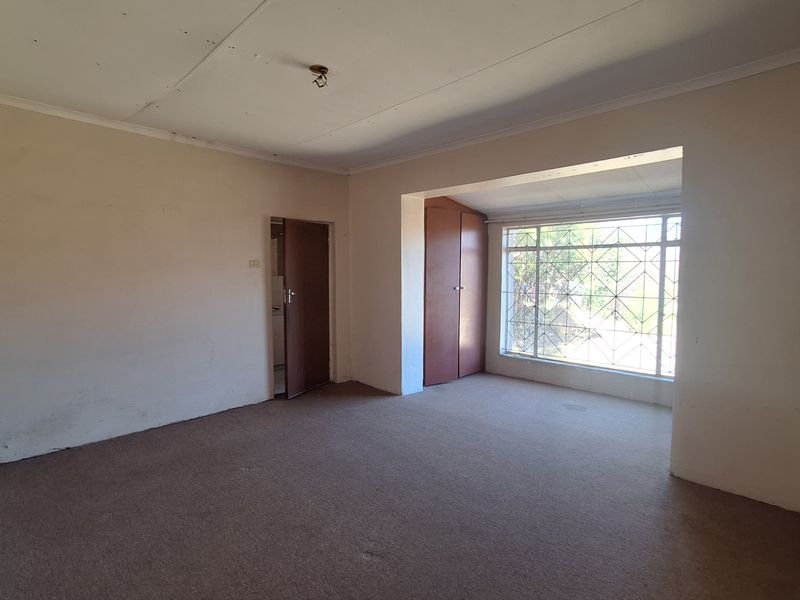 An empty living room featuring carpeted flooring, a built-in cupboard, and a window with security bars, offering a blank canvas for renovation.