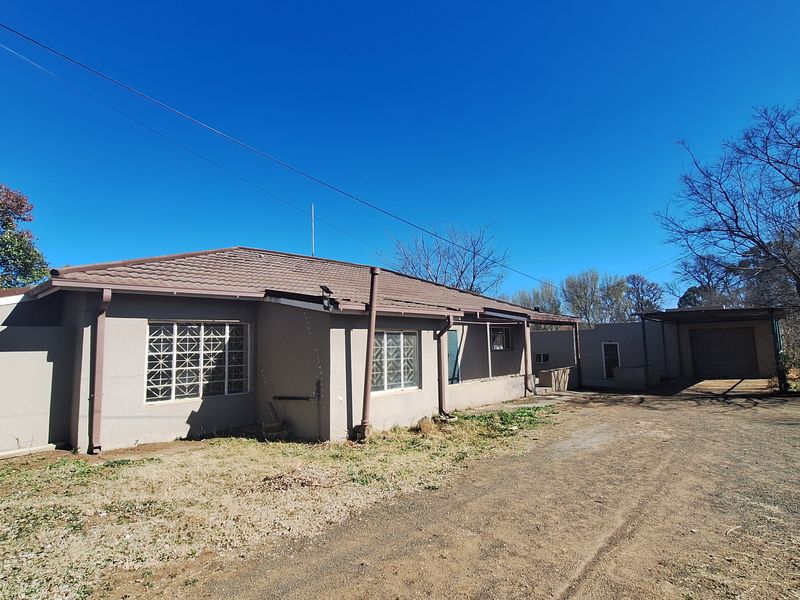 Front exterior view of a single-story house featuring a tiled roof, metal-framed windows, a garage, and an attached carport with a gravel driveway.