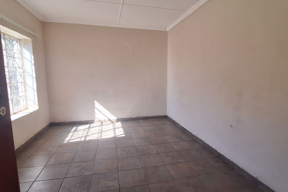 An empty bedroom featuring tiled flooring, security burglar bars on the window, and a standard ceiling finish, ready for a fresh coat of paint.