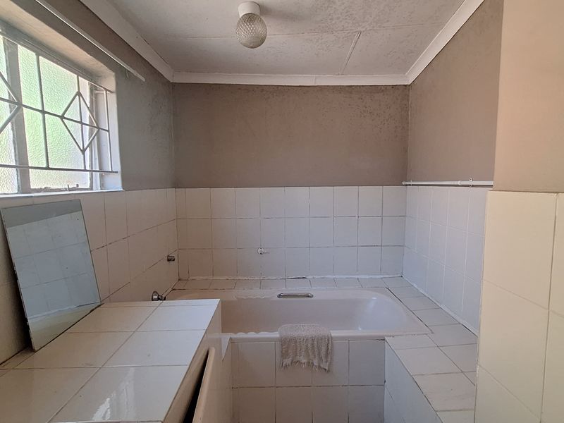 A dated bathroom featuring a built-in bathtub and tiled vanity area, requiring renovation to address wall staining and worn finishes.