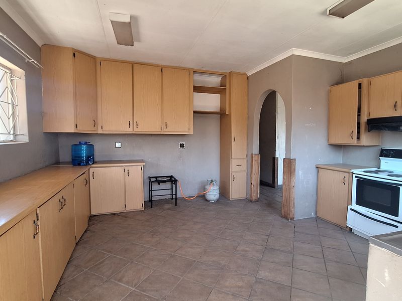 A spacious kitchen featuring laminate cabinetry, tiled flooring, and a freestanding stove, offering a functional layout with potential for modern updates.