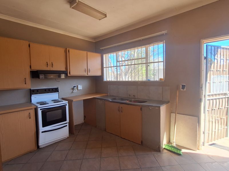 A dated kitchen featuring original cabinetry, a freestanding stove, tiled flooring, and direct access to the exterior through a security gate.