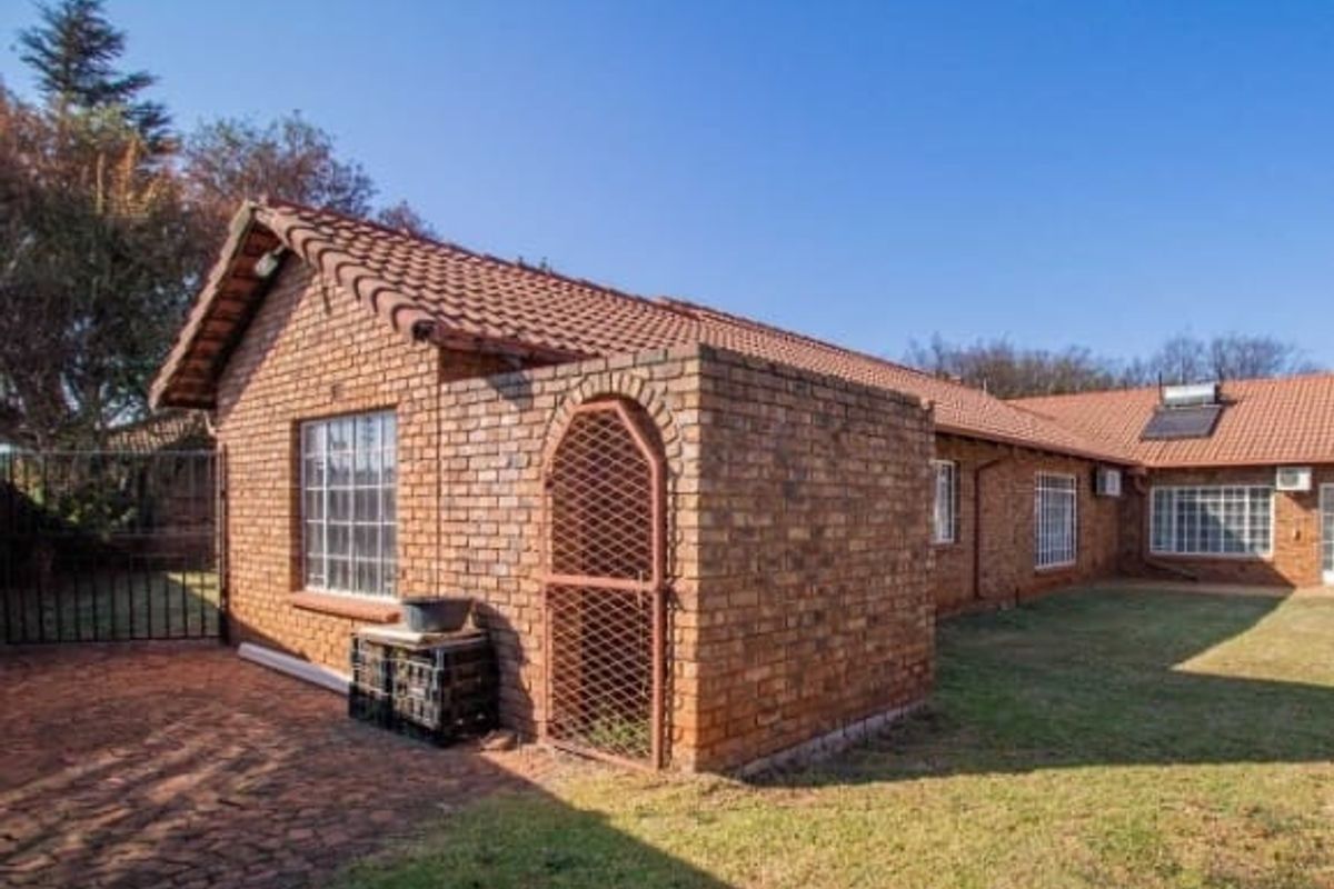 Rear view of the face brick house featuring a tiled roof, security gates, and a solar geyser system.