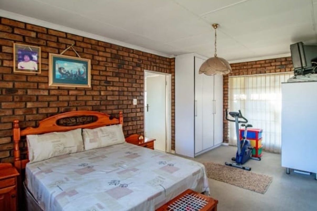 A bedroom featuring an exposed brick feature wall, built-in wardrobe storage, and neutral carpeting.