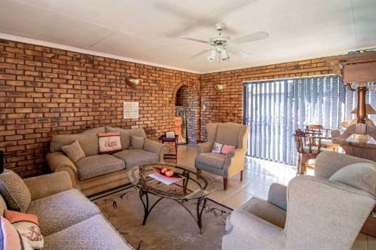 A spacious living room featuring a prominent exposed brick wall, tiled flooring, and a ceiling fan, with access to the outdoors via sliding glass doors.