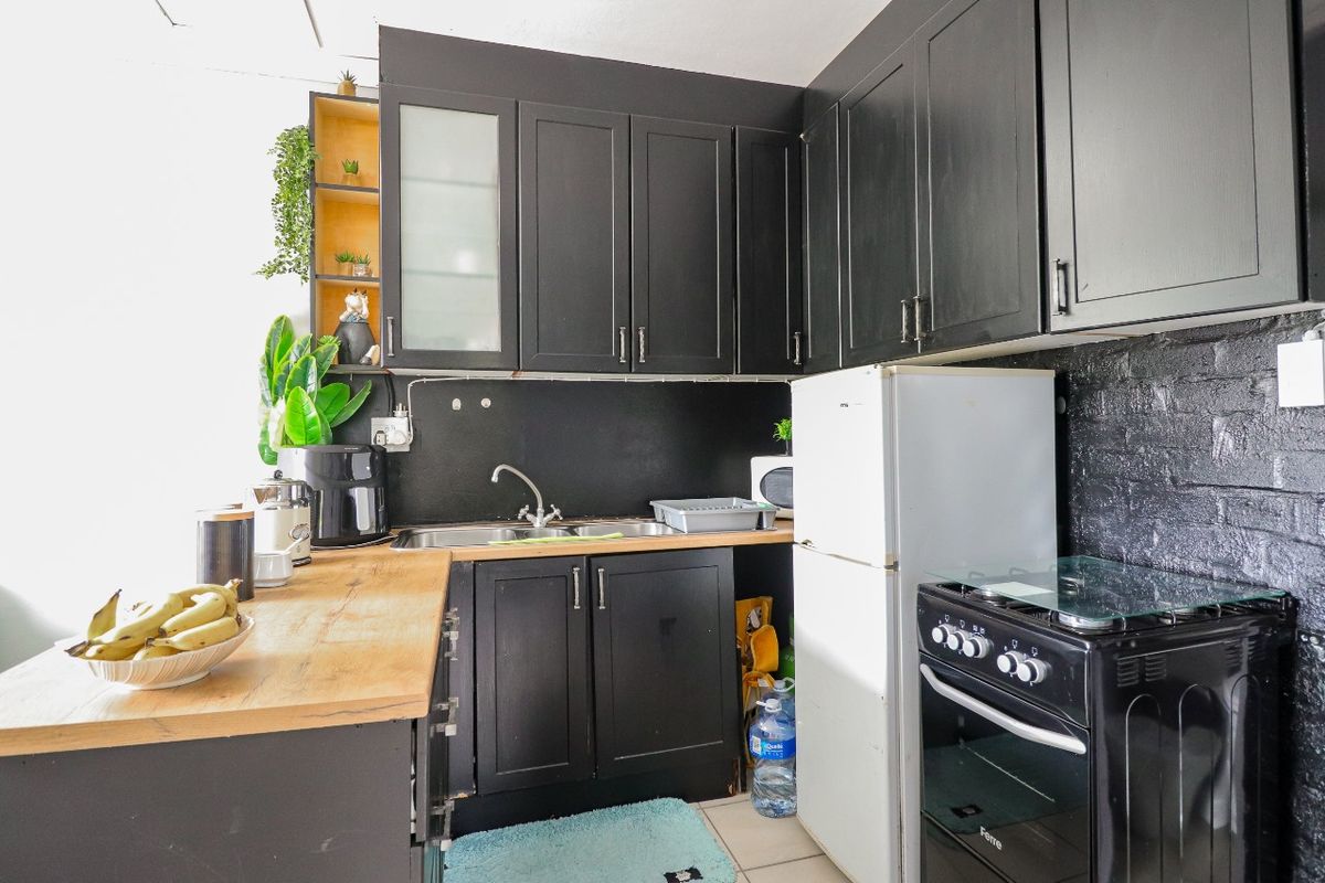 Compact kitchen featuring dark cabinetry, wooden countertops, a stainless steel sink, and a built-in oven with hob.