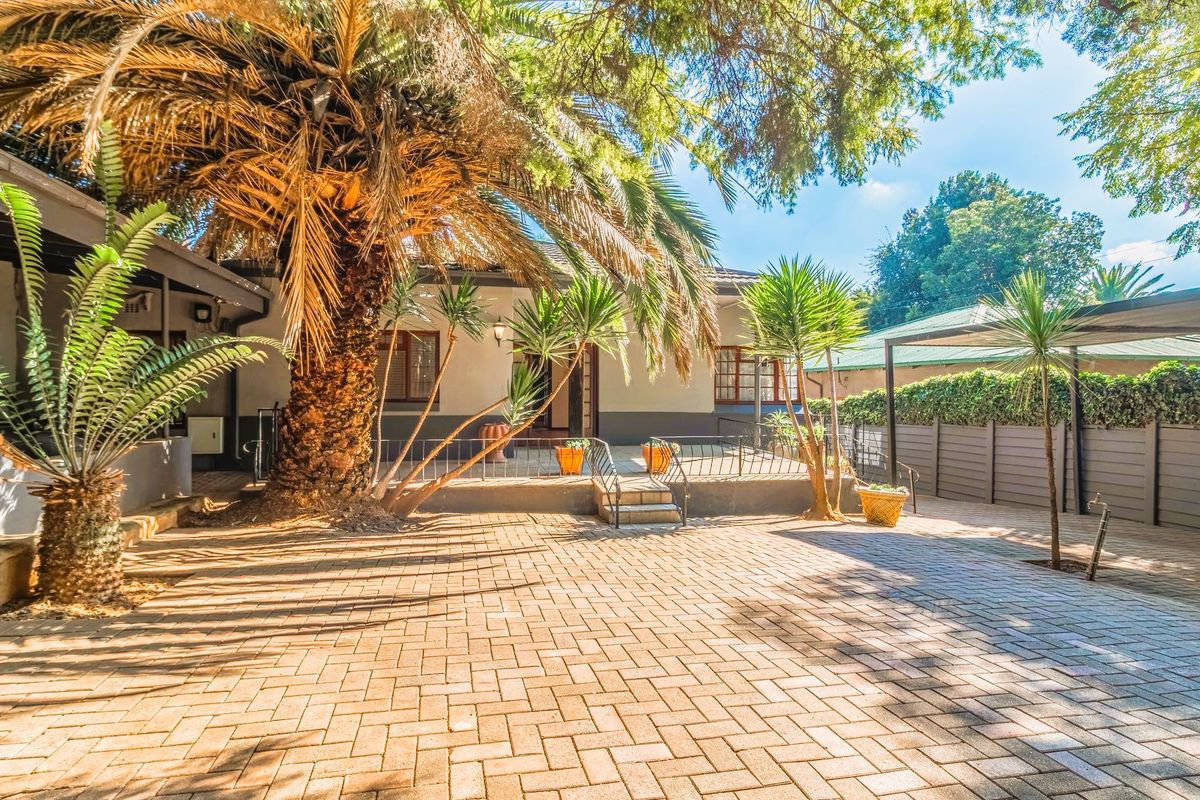 A spacious paved rear courtyard featuring a covered patio area, mature landscaping, and secure perimeter fencing.