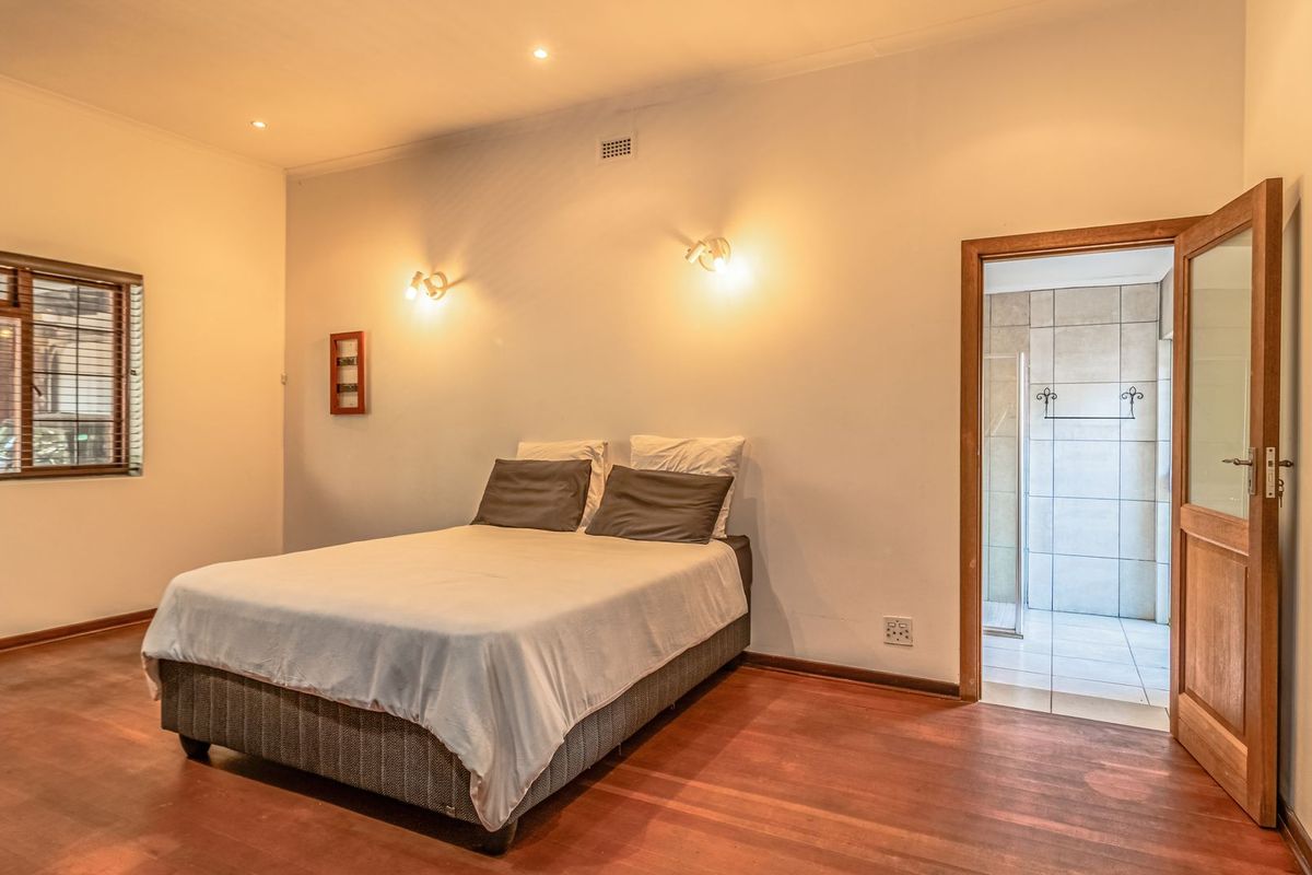 A well-maintained bedroom featuring warm timber flooring, recessed downlighting, and direct access to an en-suite bathroom.
