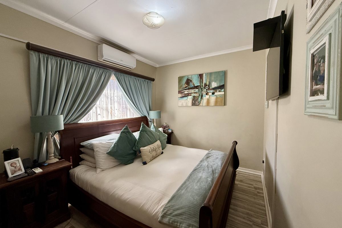 A cozy bedroom featuring wood-look flooring, a wall-mounted air conditioning unit, and a window with curtain treatments.