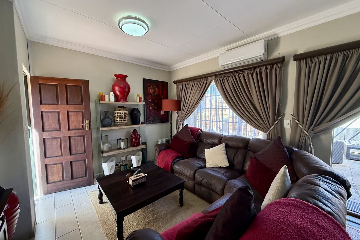 A comfortable living room featuring tiled flooring, a wall-mounted air conditioning unit, and large windows with curtains.