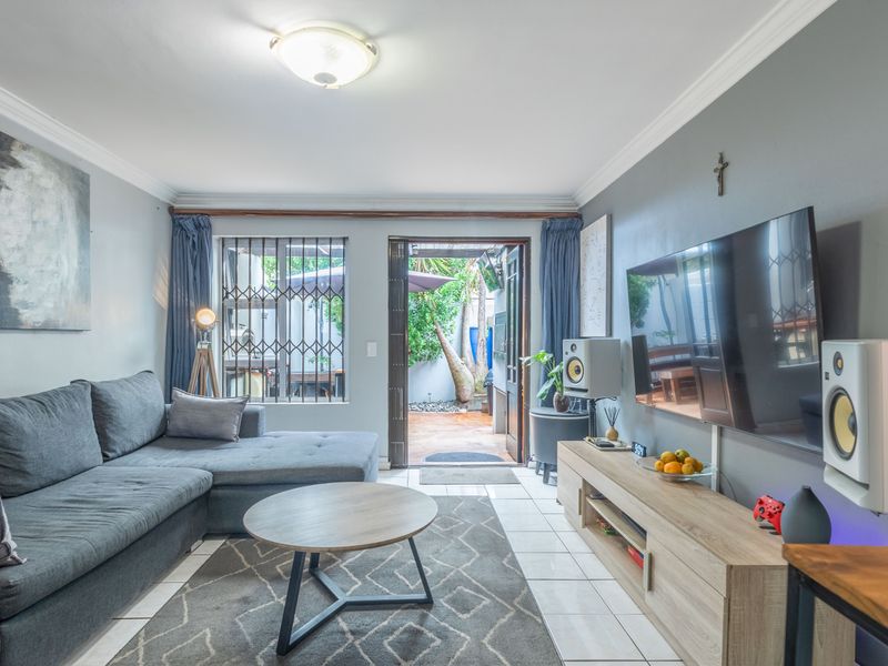 A well-maintained living room featuring tiled flooring, crown molding, and direct access to an outdoor patio area through a secure sliding door.