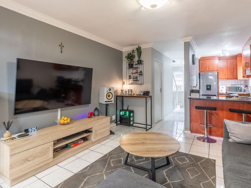 Open-plan living and kitchen area featuring tiled flooring, wooden cabinetry, and a breakfast bar, creating a functional and connected living space.