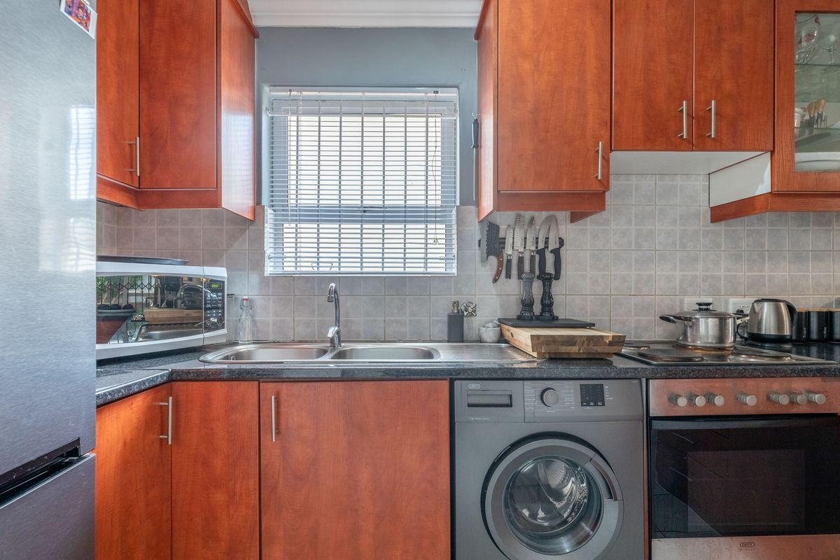 A functional kitchen featuring wood-finish cabinetry, tiled backsplash, integrated washing machine, and built-in oven with hob.